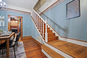 A dining area with a wooden table and chairs, a staircase with wooden steps and white railings, and a wall with a geometric pattern. - Spacious 5BR Home in Meridian (Meridian)