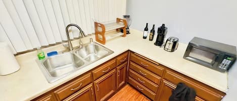 Una cocina con un lavamanos doble, armarios de madera, un microondas y un tostador.