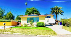 A single-story house with a red roof, a small front yard, and a parked RV in the driveway.