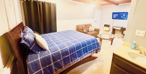 A hotel room with a bed, a sofa, a small table, a TV, and a bathroom.