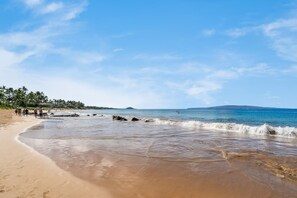Ein Strand mit blauem Himmel, ruhigem Wasser und einem fernen Berg.