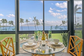 A table set for two with a bottle of wine, two chairs, and a view of the ocean and palm trees. - Updated Beachfront 1BD w Ocean Views - Kihei Surfside 306 (Kihei)