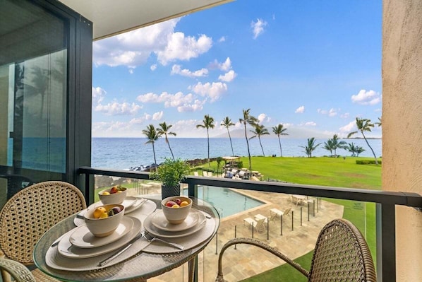 A balcony with a table set for breakfast, overlooking a pool and a golf course. - Updated Beachfront 1BD w Ocean Views - Kihei Surfside 306 (Kihei)