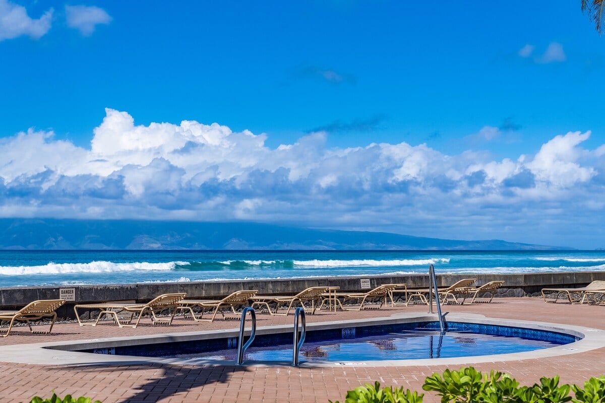 A pool area with lounge chairs and a view of the ocean.
