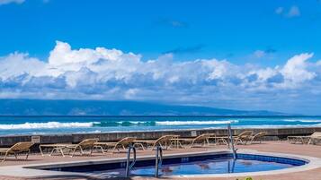 A pool area with lounge chairs and a view of the ocean.