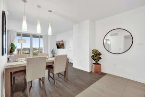 A modern dining area with a wooden table, chairs, pendant lights, and a large window. - Condo Resort Hallandale| Ocean and Canal View (Hallandale Beach)