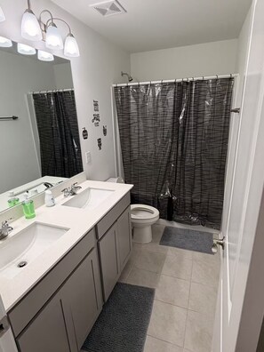 A modern bathroom with two sinks, a toilet, a shower with a patterned curtain, and a mirror with wall stickers. - Beautiful Modern Home Near I-65 - Near Nashville (White House)