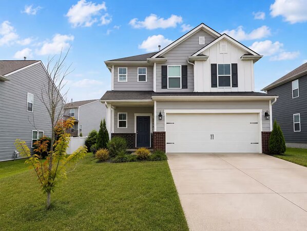 A two-story residential house with a front garage, a small front yard, and a clear sky. - Beautiful Modern Home Near I-65 - Near Nashville (White House)