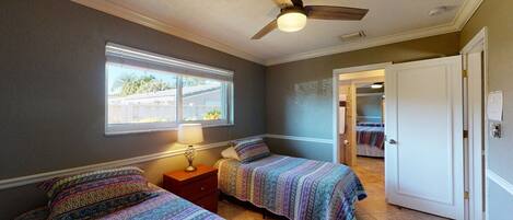A bedroom with two beds, a ceiling fan, a window, and a door leading to another room.