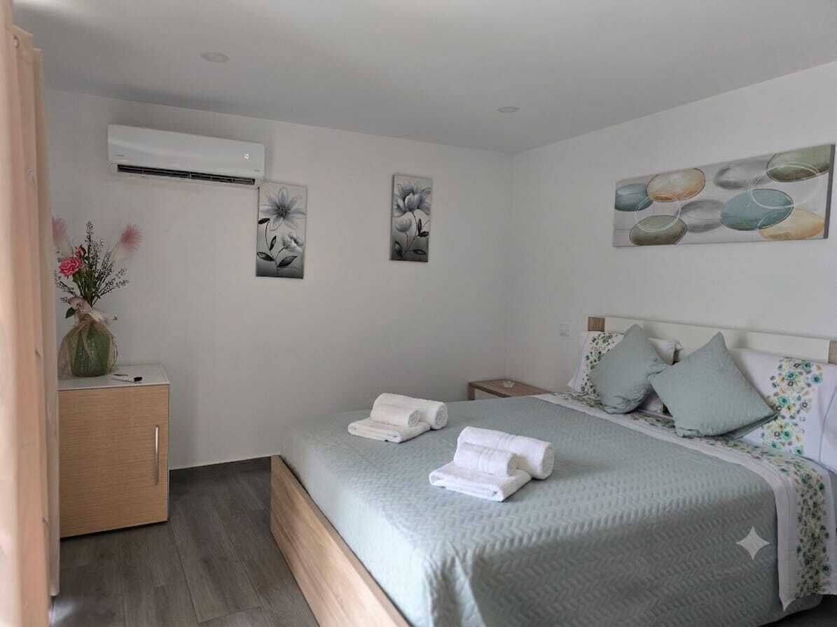 Een slaapkamer met een bed, een nachtkastje, een wandairconditioner en twee decoratieve schilderijen.