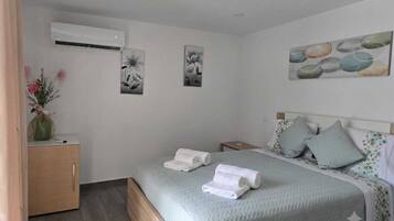Een slaapkamer met een bed, een nachtkastje, een wandairconditioner en twee decoratieve schilderijen.