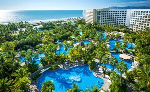 A resort with multiple swimming pools surrounded by palm trees and a beach view.