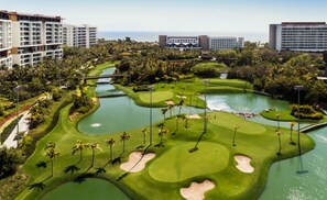 A golf course with bunkers, water hazards, and palm trees.