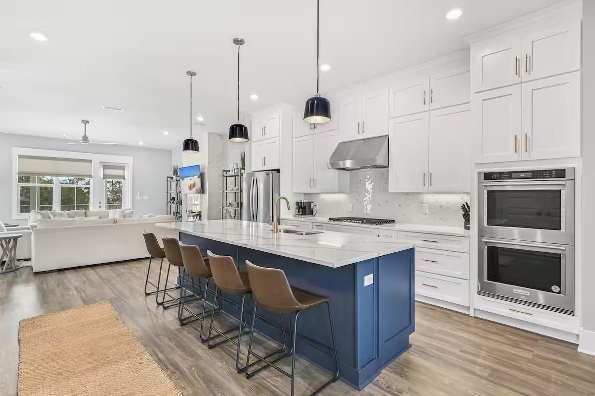 Une cuisine moderne avec des meubles blancs, un îlot central bleu, des appareils en acier inoxydable et des luminaires suspendus.