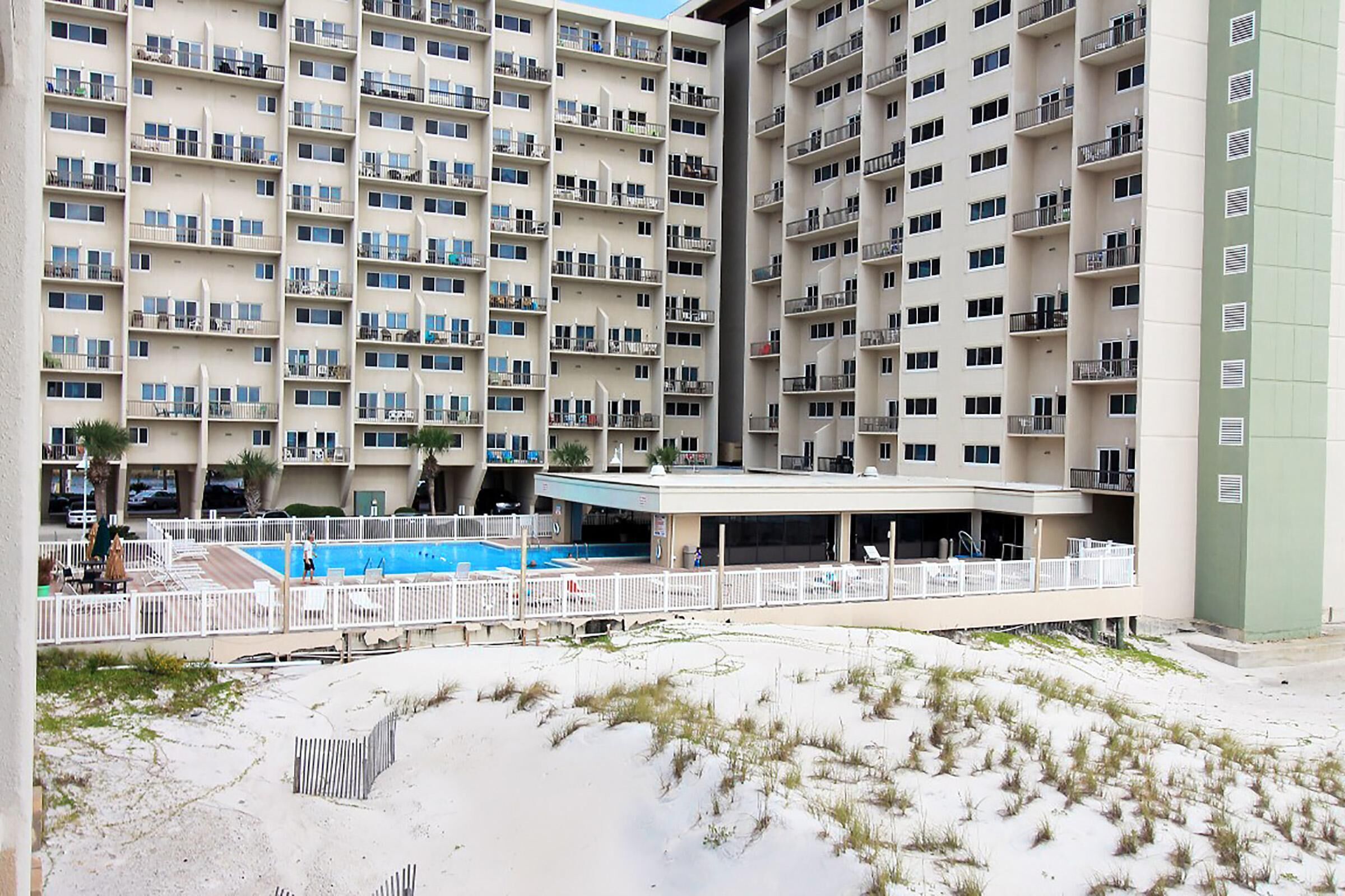 A high-rise hotel with multiple balconies, a swimming pool, and a covered outdoor area.
