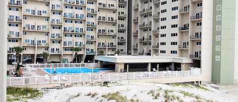 A high-rise hotel with multiple balconies, a swimming pool, and a covered outdoor area.