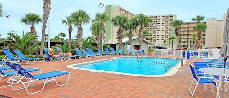 Un espace piscine avec des chaises longues bleues et des palmiers.
