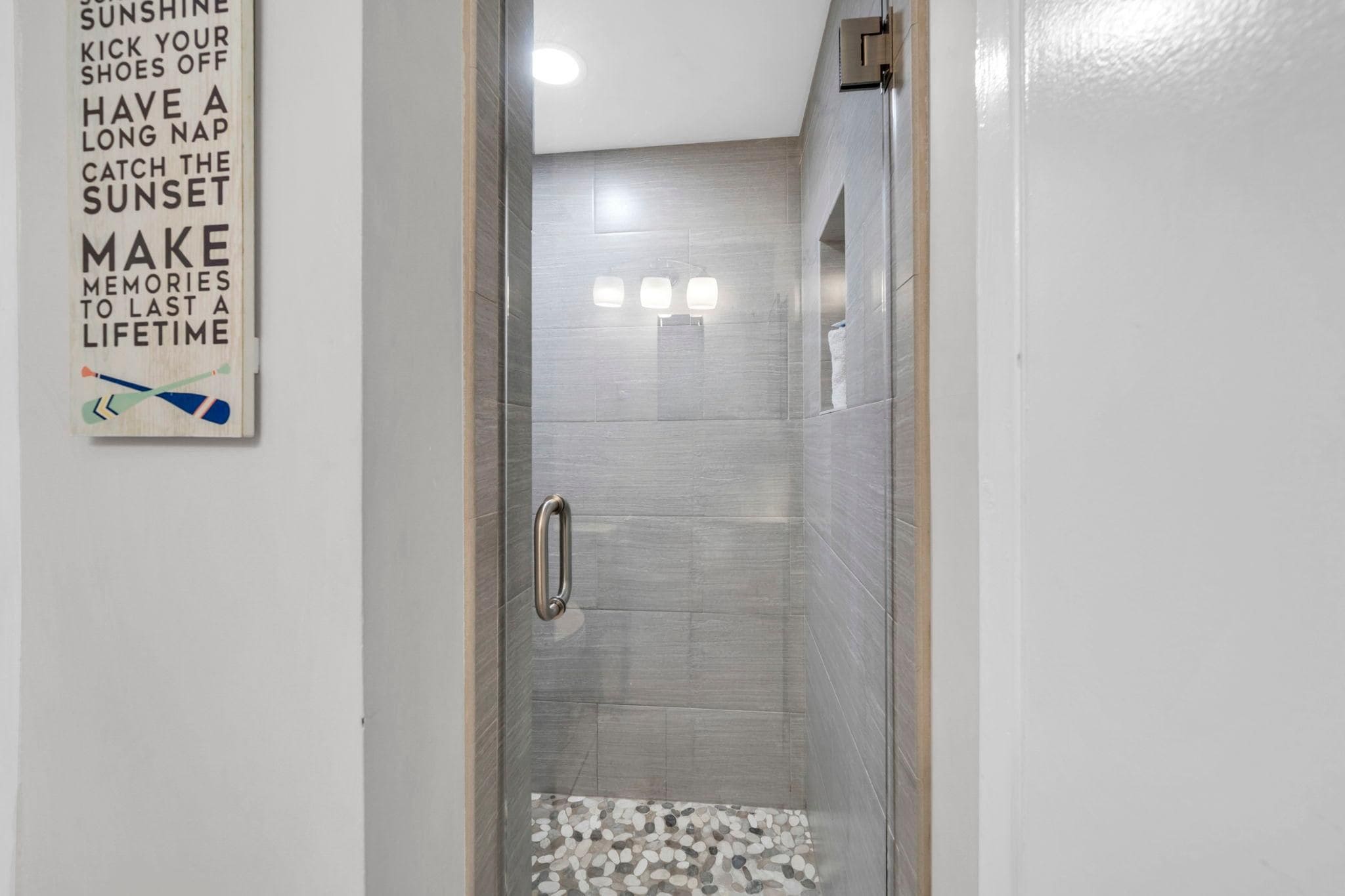 Un espacio de ducha con puerta de vidrio, un perchero y una frase motivadora en la pared.