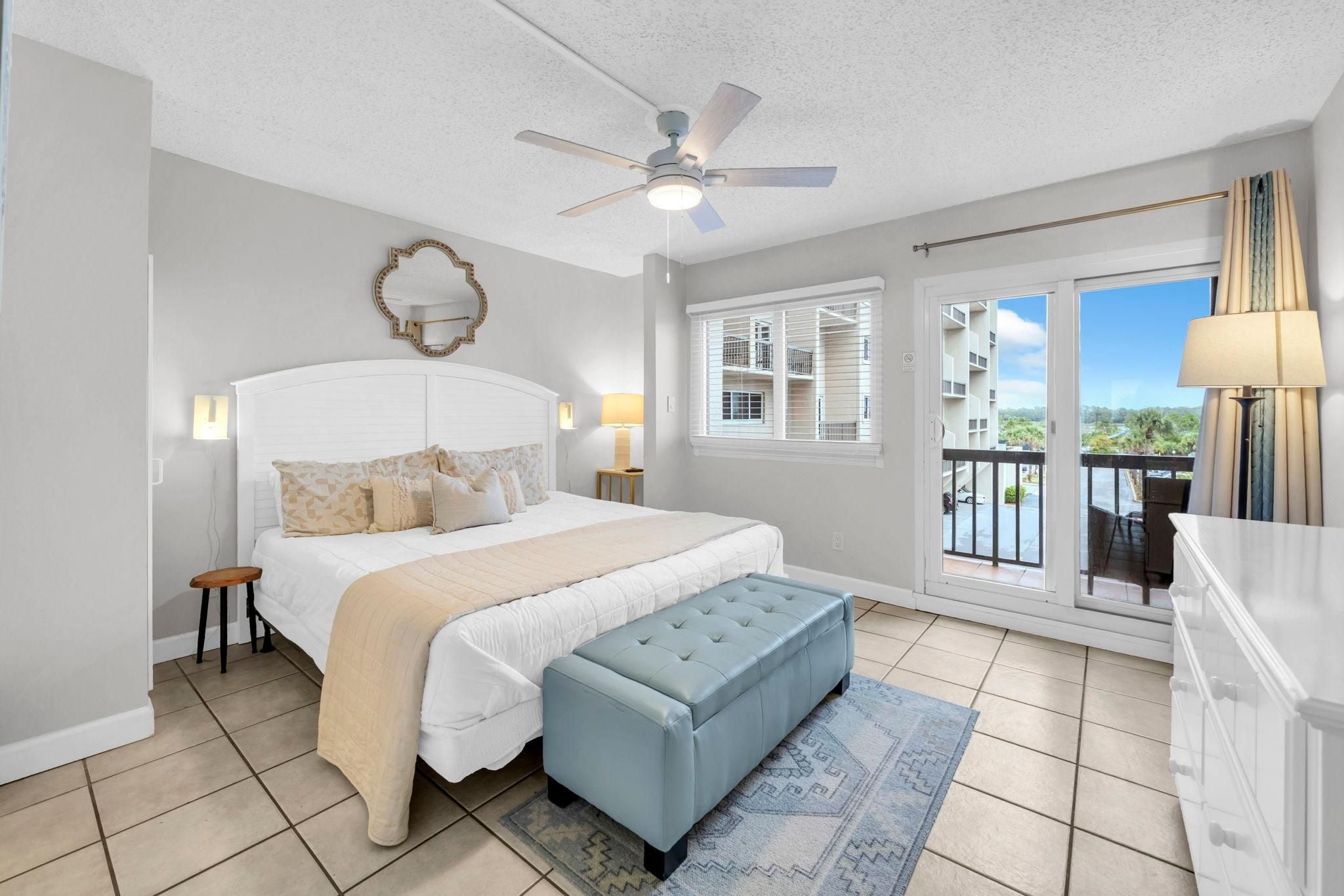 Une chambre à coucher avec un lit, un ventilateur de plafond, une fenêtre avec des stores, un balcon et une vue sur l’extérieur.