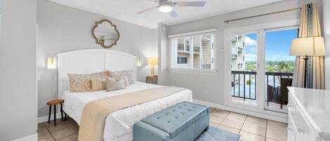 Une chambre à coucher avec un lit, un ventilateur de plafond, une fenêtre avec des stores, un balcon et une vue sur l’extérieur.