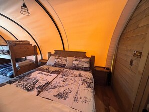 Una cama individual con cabecera de madera y colcha estampada en una habitación con techo curvo y paredes de madera.