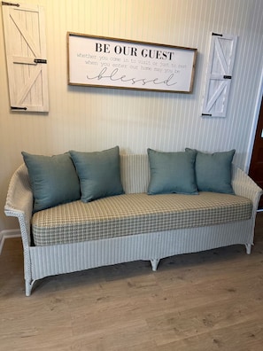 A wicker sofa with two cushions against a wall with vertical stripes and two white doors with black handles.