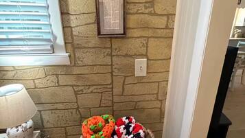Une pièce avec un mur en pierre, une plaque commémorative encadrée, un panier rempli d’objets colorés faits au crochet et une lampe posée sur une table.