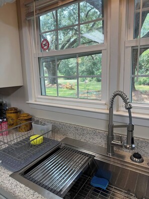 Een keuken met een roestvrijstalen spoelbak, een raam met een 'Niet roken'-bord en uitzicht op een groen landschap.