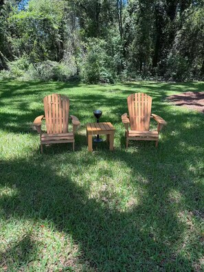 Dos sillas de madera tipo Adirondack y una mesita con un cuenco sobre un césped.