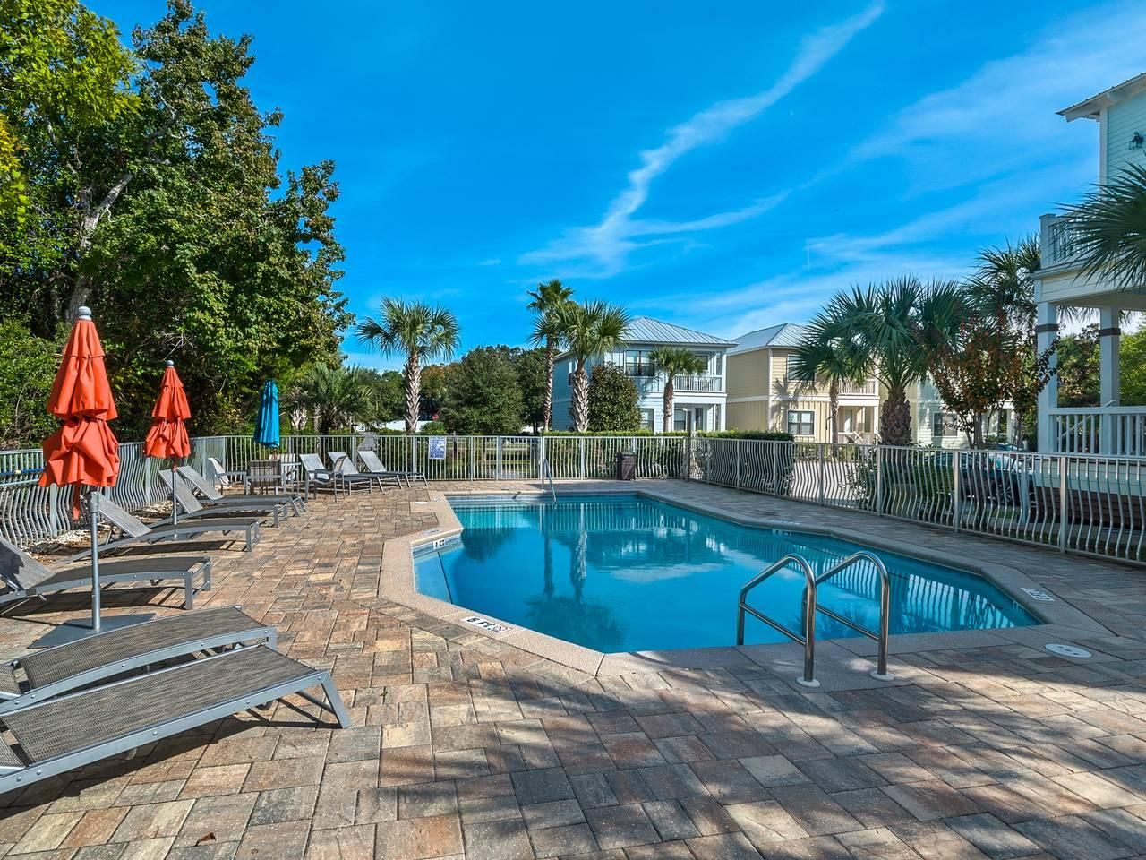 A swimming pool with lounge chairs and umbrellas, surrounded by a fence and trees.