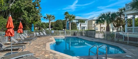 A swimming pool with lounge chairs and umbrellas, surrounded by a fence and trees.