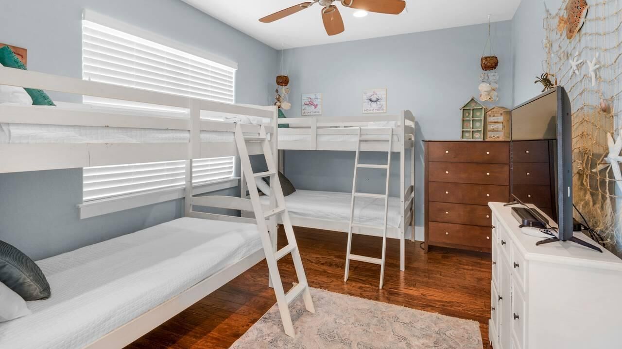 A bunk bed room with a ladder, a dresser, and a ceiling fan.
