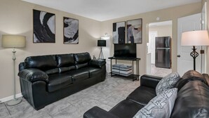A living room with a black leather sofa, a TV stand with a flat-screen TV, and abstract wall art. - Cozy 2BR Near Prisma | Minutes to Downtown (Columbia)