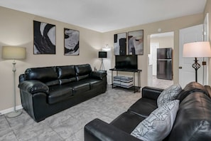 Una sala de estar con un sofá de cuero negro, un mueble para televisor con televisor de pantalla plana y arte abstracto en la pared.