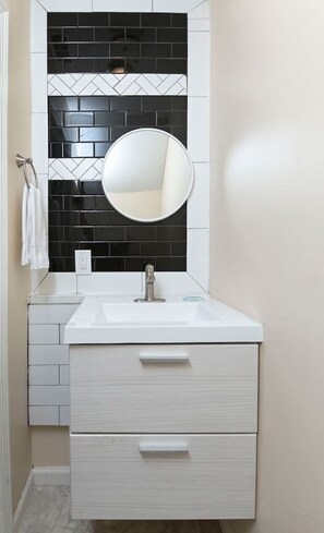 Un baño con un lavamanos blanco, un espejo redondo y un salpicadero de azulejos blanco y negro.