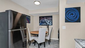 A compact kitchen with a refrigerator, dining table, chairs, and artwork on the walls. - Cozy 2BR Near Prisma | Minutes to Downtown (Columbia)