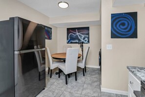 Cocina compacta con refrigerador, mesa de comedor, sillas y obras de arte en las paredes.
