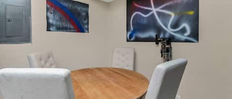 Une salle de conférence avec une table ronde en bois, quatre chaises rembourrées et deux tableaux abstraits accrochés aux murs.