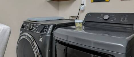 A laundry room with a front-loading washer and dryer, a white cabinet above, and artwork on the wall.
