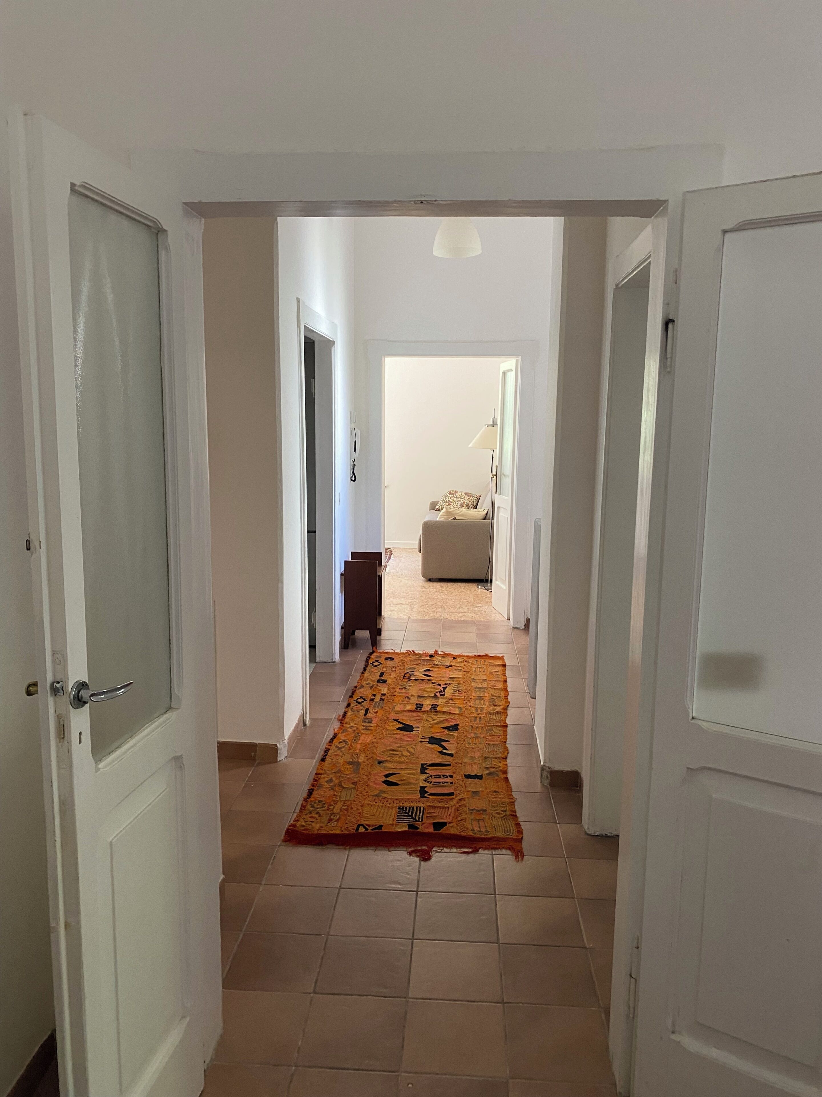 Un corridoio con porte bianche, un tappeto decorato e un divano in lontananza.