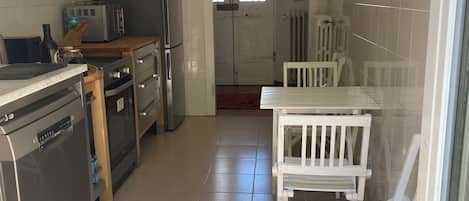 A compact kitchen with a dishwasher, stove, microwave, and a dining area with white chairs.