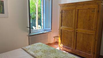 Una camera da letto con un letto, un armadio in legno, un termosifone e una finestra vista alberi e una panchina all'esterno.