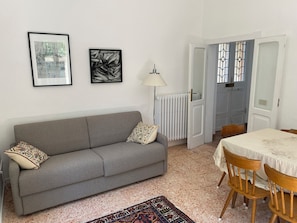 A living room with a grey sofa, a patterned rug, a dining table with chairs, and two framed artworks on the wall. - Porzione di villa con giardino privato e A/C (Senigallia)