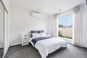 Ein Schlafzimmer mit einem Bett, einem Nachttisch, einem Fenster mit Vorhängen und einem Deckenventil.