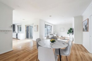 Eine moderne Küche mit weißen Schränken, einem eingebauten Ofen und einem Essbereich mit einem Marmortisch und grauen Stühlen.
