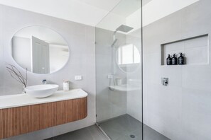Ein modernes Badezimmer mit einem großen runden Spiegel, einem weißen Waschbecken und einer Duschkabine aus Glas.