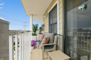 A balcony with a cushioned seating area, a potted plant, and a window with a view of a building.