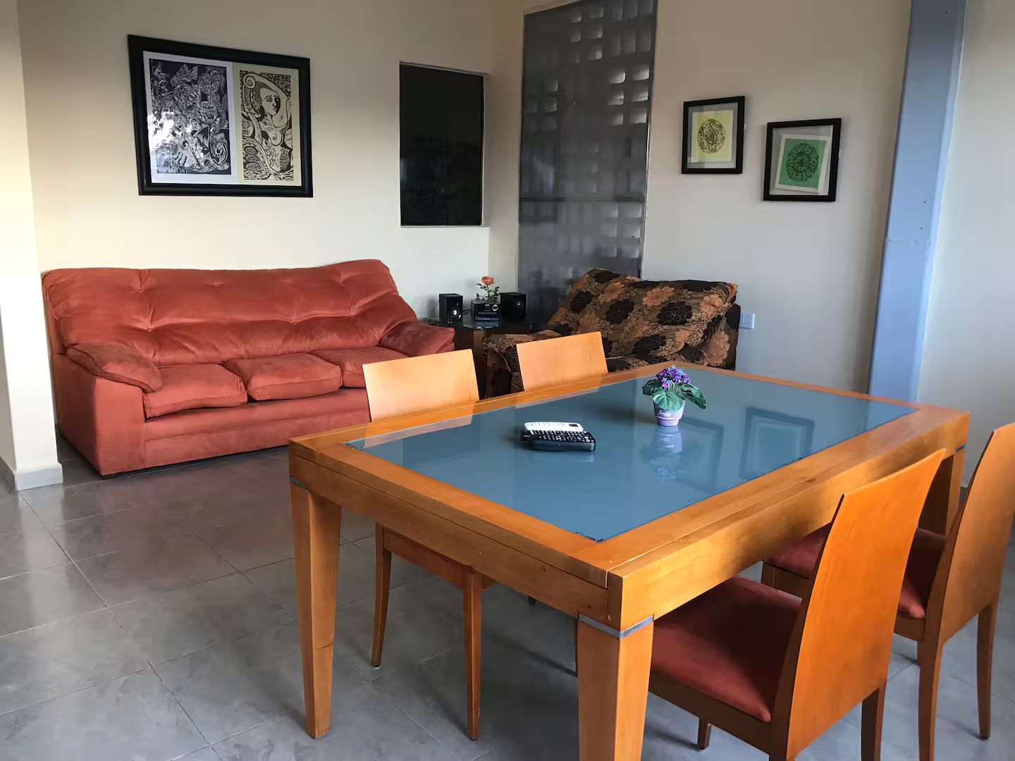 Ein Wohnzimmer mit einem roten Sofa, einem Esstisch mit Glasplatte und Holzstühlen.