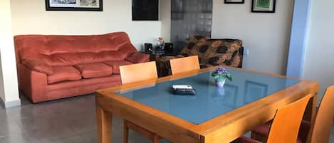 Ein Wohnzimmer mit einem roten Sofa, einem Esstisch mit Glasplatte und Holzstühlen.