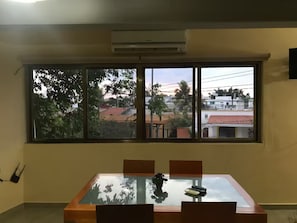 Ein Zimmer mit großem Fenster, einem Tisch mit Stühlen und einer Klimaanlage.